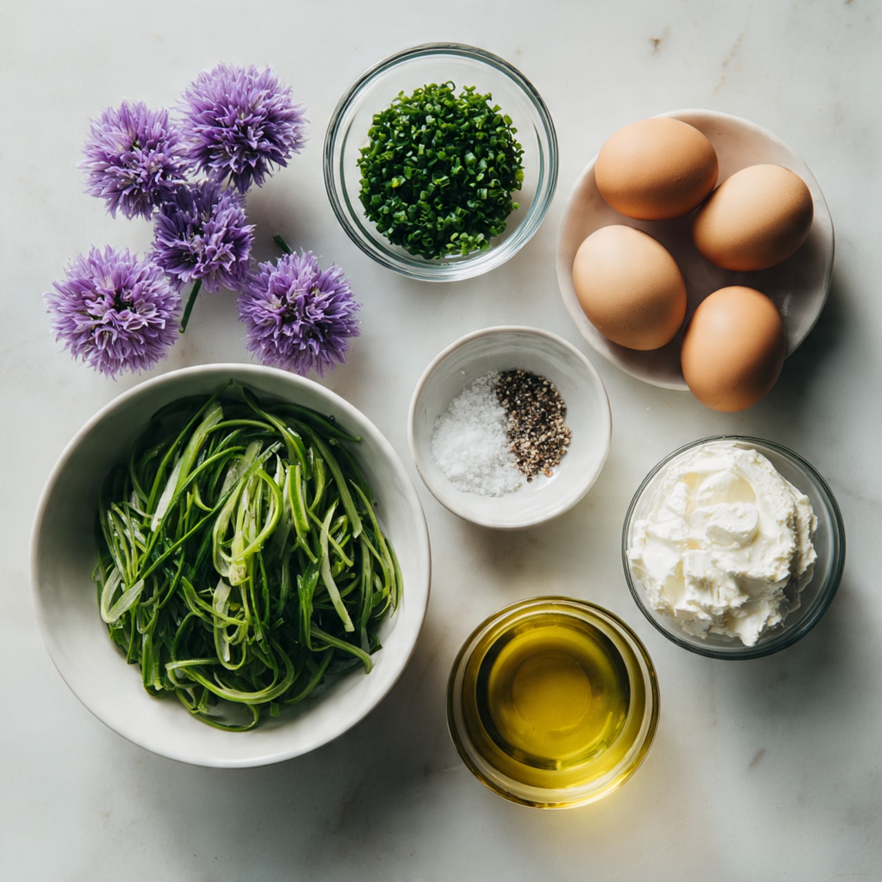 The image shows a flat lay on a white marbled surface with seven fresh ingredients arranged neatly. In the center bottom, there is a white bowl filled with thin, long, bright green vegetable strips. Above it on the left, there are two small purple flowers placed close together. To the right of the flowers, three smooth brown eggs are arranged in a triangle shape. Above the eggs, there is a small clear glass bowl filled with finely chopped dark green chives. To the right of the chives, a small clear glass bowl holds a soft, white creamy cheese. Below it, a small white bowl contains coarse salt mixed with crushed black pepper. At the bottom right corner, a small clear glass bowl is filled with golden-yellow olive oil. Photo taken with an iphone --ar 4:5 --v 7