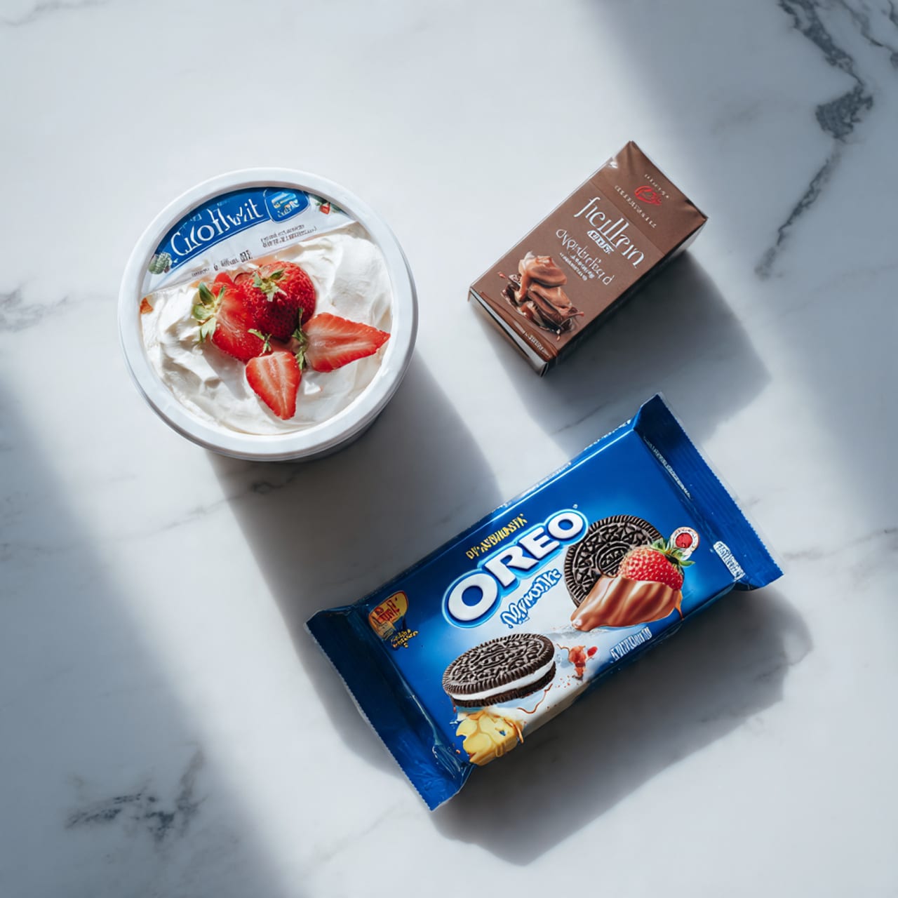 The image shows three unopened food packages placed on a white marbled surface. At the top left is a round tub of Cool Whip whipped topping with a blue lid and white container, featuring an image of whipped cream and strawberries on the label. Next to it on the right is a small rectangular box of Jell-O chocolate flavor in brown packaging with a picture of chocolate pudding on the front. Below these two, there is a large rectangular package of Oreo cookies, mainly blue with some red and yellow, showing an Oreo cookie image and Canadian-themed graphics. photo taken with an iphone --ar 4:5 --v 7