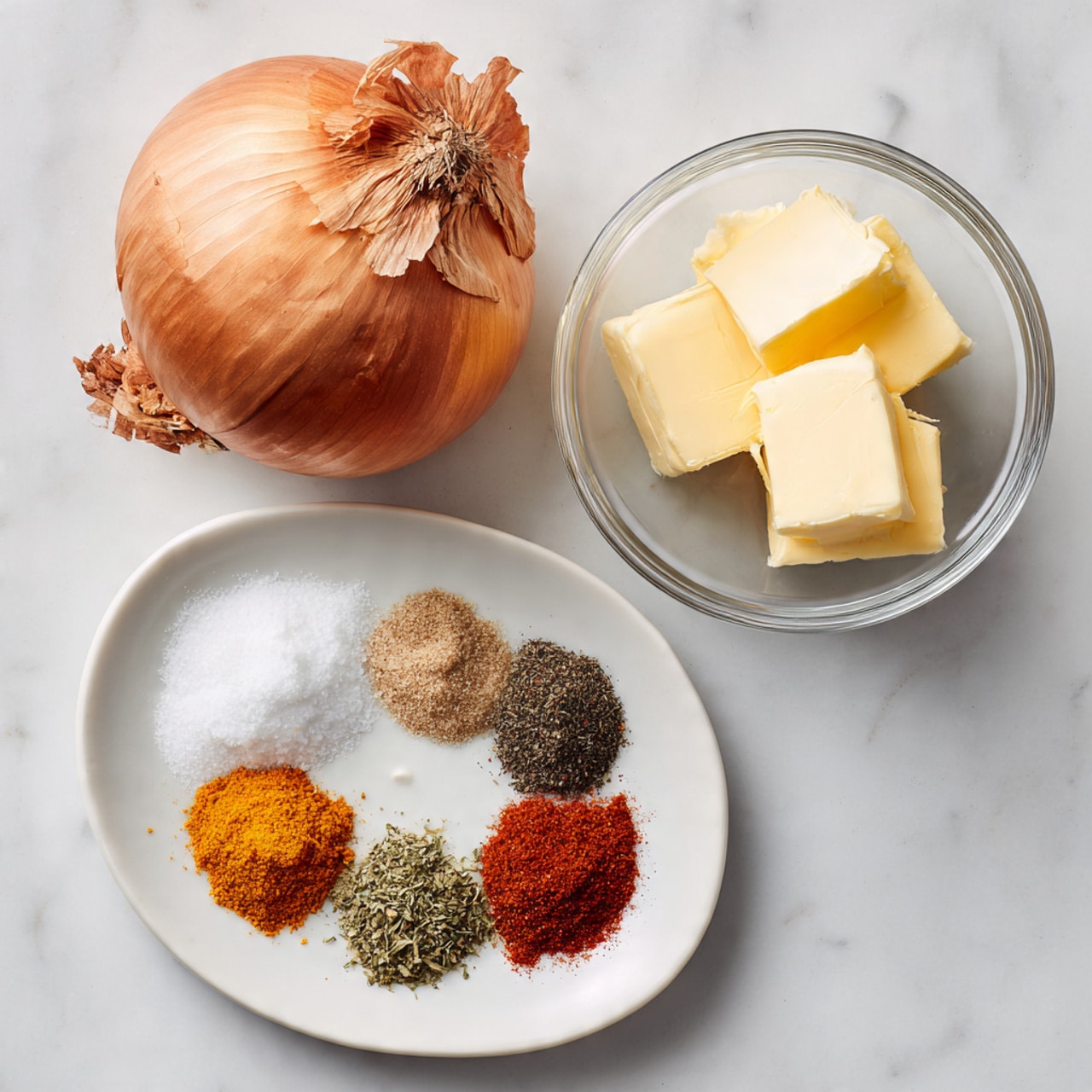 The image shows a whole brown onion with its dry skin partly peeling, placed at the top left on a white marbled surface. Below it, there is a small white plate holding six separate piles of spices and herbs in different colors and textures: coarse white salt, black pepper, orange-red spice, green dried parsley, white powder, and a reddish-brown spice. To the right of the onion and spices, there is a small clear glass bowl with two pieces of pale yellow butter. photo taken with an iphone --ar 4:5 --v 7