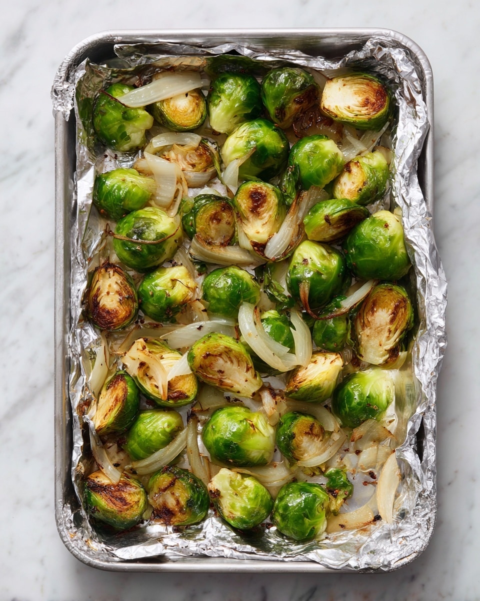 The image shows a foil-lined tray with roasted Brussels sprouts cut in half, scattered evenly across the surface. The Brussels sprouts have a bright green color with some browned and slightly crispy edges. Mixed among the sprouts are thin slices of cooked onions, which are white and translucent with slight browning. The tray rests on a white marbled surface, and the foil has wrinkled edges with some browned spots from cooking. photo taken with an iphone --ar 4:5 --v 7