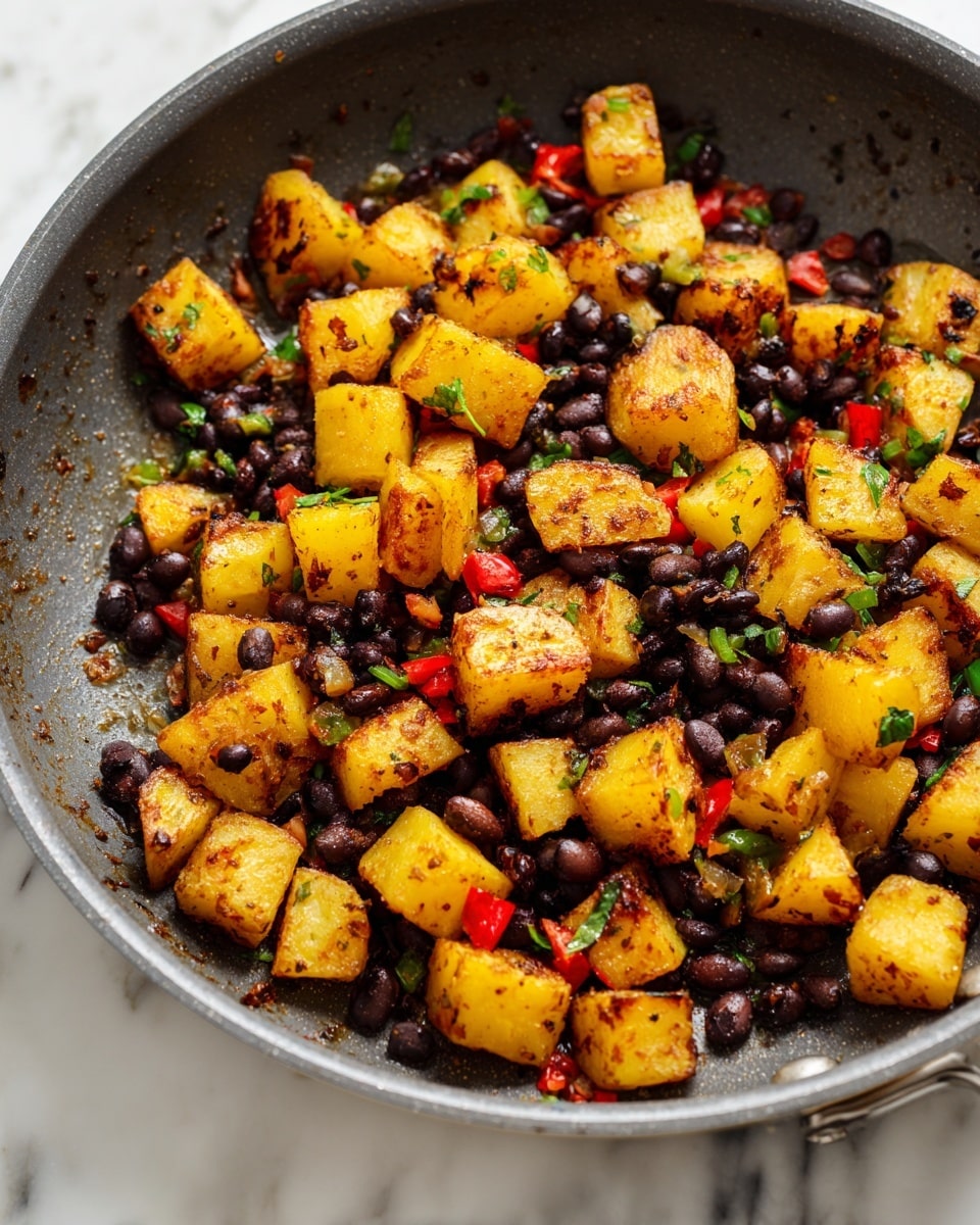 A close-up of a frying pan filled with cooked potato pieces and black beans. There are large chunks of golden-yellow potatoes with browned edges scattered evenly across the pan, mixed with small dark brown beans. Small bits of red and green peppers are interspersed among the potatoes and beans, adding pops of color. The pan is a dark gray color with a slight oily sheen, and there is a white marbled surface below it. photo taken with an iphone --ar 4:5 --v 7