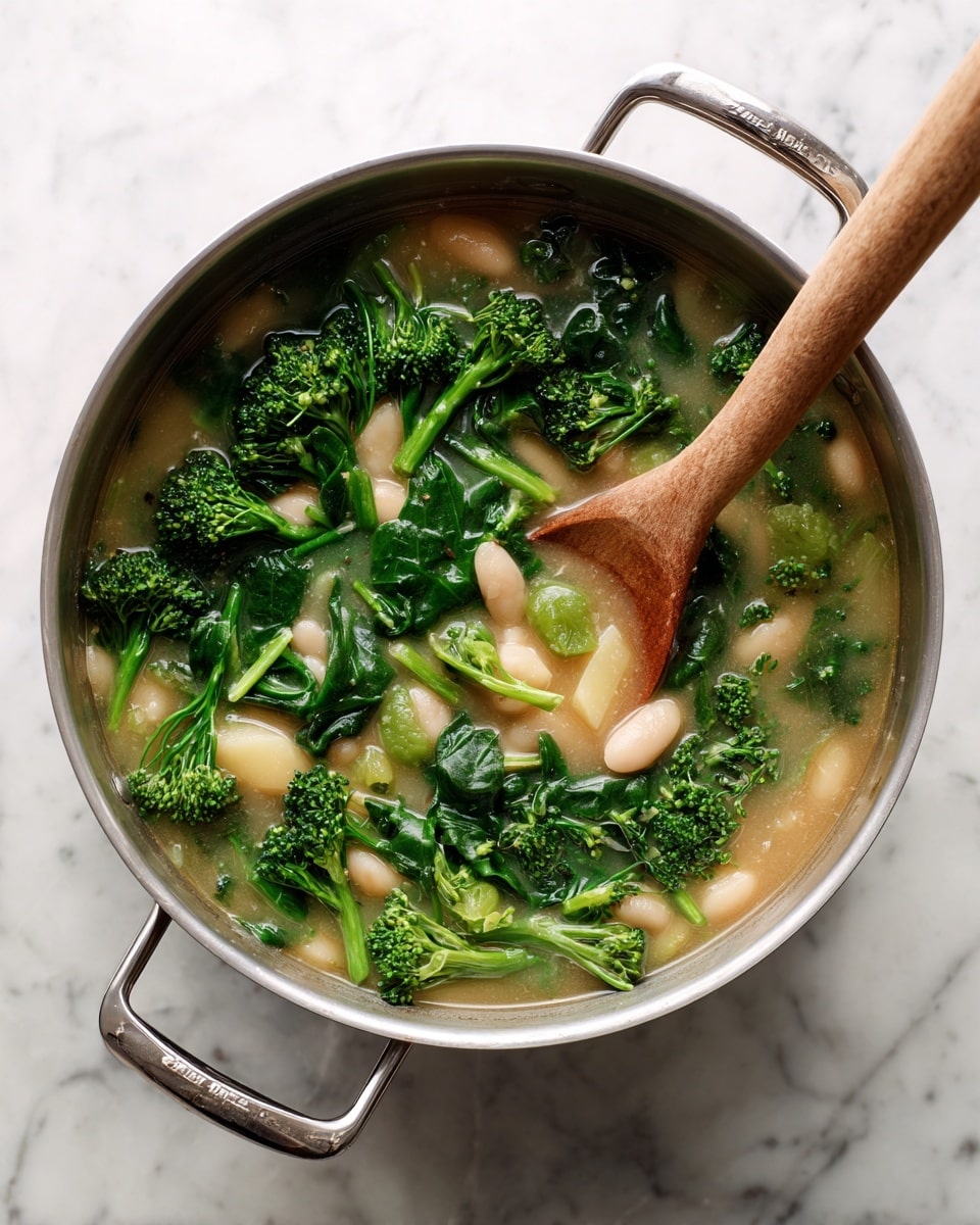 A large silver pot filled with a soup showing three main layers: the bottom light beige, soft and creamy broth, the middle vibrant dark green spinach leaves overlapping with small bright green broccoli florets scattered throughout, and pale white beans and translucent potato chunks evenly mixed in. A light wooden spoon lies inside the pot, partially submerged in the soup, stirring the ingredients. The pot is set on a white marbled surface, steam faintly rising, with the pot handles on each side clearly visible. Photo taken with an iphone --ar 4:5 --v 7