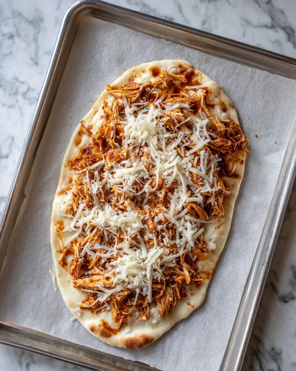 The image shows a small, oval-shaped flatbread placed on parchment paper on a metal tray. The flatbread is topped with a layer of shredded orange chicken, evenly spread across the surface, and a layer of shredded white cheese scattered on top. The flatbread has some light brown spots indicating it’s cooked but still soft in texture. The background is a white marbled surface. photo taken with an iphone --ar 4:5 --v 7