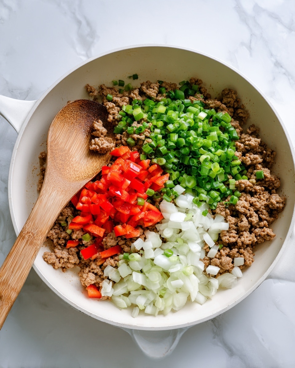 The image shows a white pan on a white marbled surface, containing a mix of cooked ground meat, chopped green onions, red bell peppers, and white onions. The ingredients are layered evenly inside the pan, with the ground meat forming the main base, scattered bits of red bell peppers and chopped green onions brightly spread across the top, and finely chopped white onions clustered in one section. A wooden spoon rests inside the pan, partly covered by the mixture, giving a sense of ongoing cooking. Photo taken with an iphone --ar 4:5 --v 7