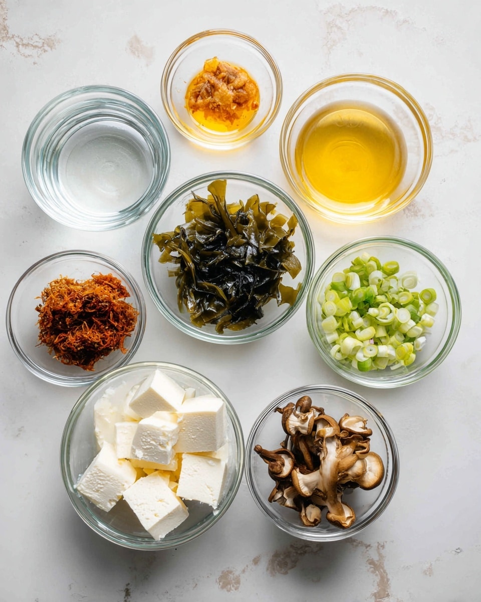 The image shows seven small glass bowls arranged on a white marbled surface. The top row has three bowls: the left one holds a clear liquid, the middle one has a small amount of orange liquid, and the right one contains a yellow liquid. Below and to the left is a bowl filled with sliced brown and white mushrooms. To its right is a bowl with white tofu cubes. Next to the tofu is a bowl with green chopped scallions and two dark green seaweed sheets resting inside. Above this bowl is a small bowl with a brown paste. The colors vary from clear, orange, yellow, brown, green, white, to dark green textures, each layered simply in their own bowls. photo taken with an iphone --ar 4:5 --v 7