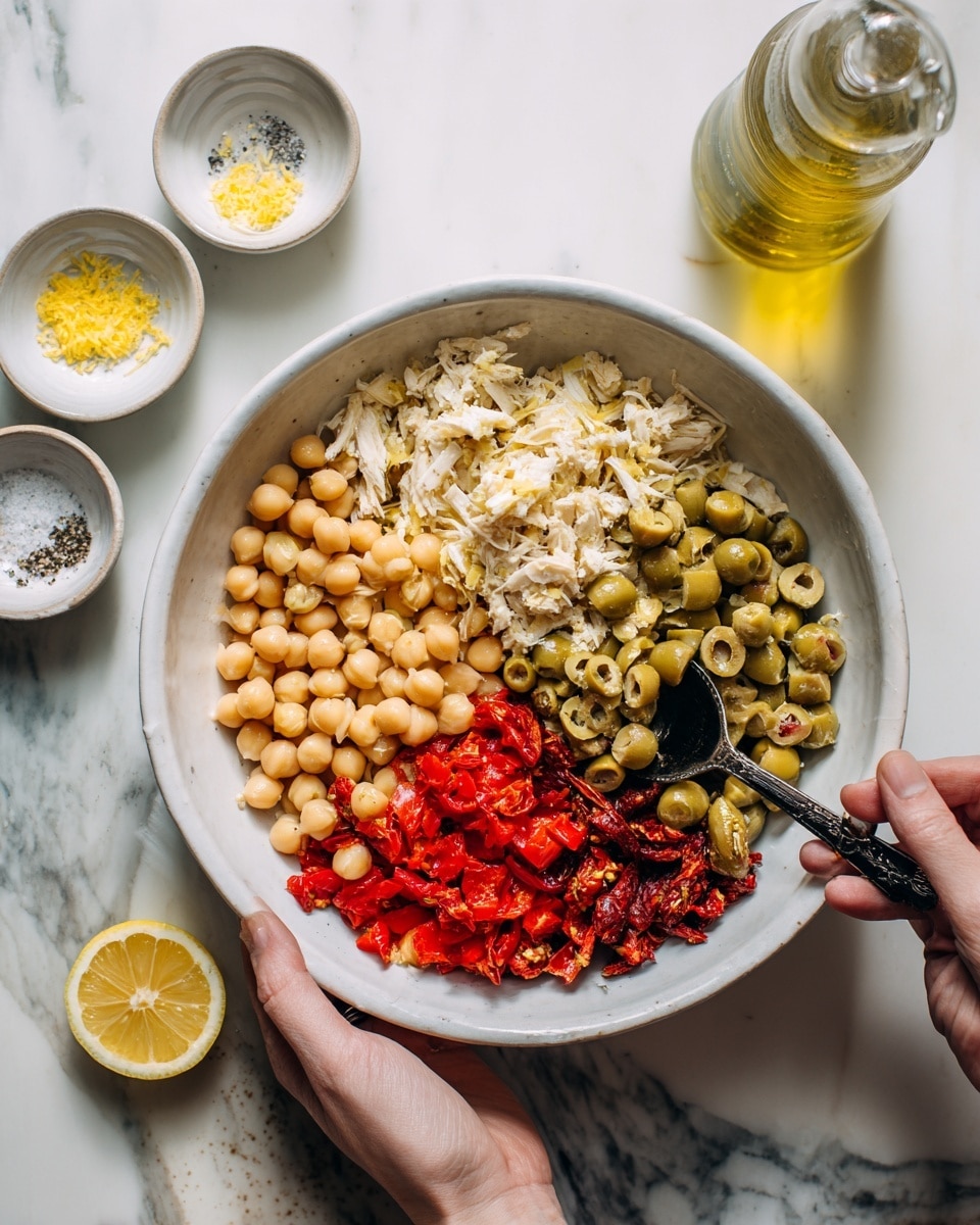 A white bowl sits on a white marbled surface, filled with four distinct layers: the bottom left layer is made of pale yellow chickpeas, the bottom right has bright red diced roasted peppers, the top left consists of shredded white chicken, and the top right features chopped green olives mixed with sun-dried tomatoes. A woman's hand holds the bowl on the left side, while another woman's hand uses a black spoon to mix the olives and chicken on the right side. Nearby on the marble background, there are small white dishes with salt and pepper, lemon zest, half a lemon, and a glass bottle of olive oil. Photo taken with an iphone --ar 4:5 --v 7