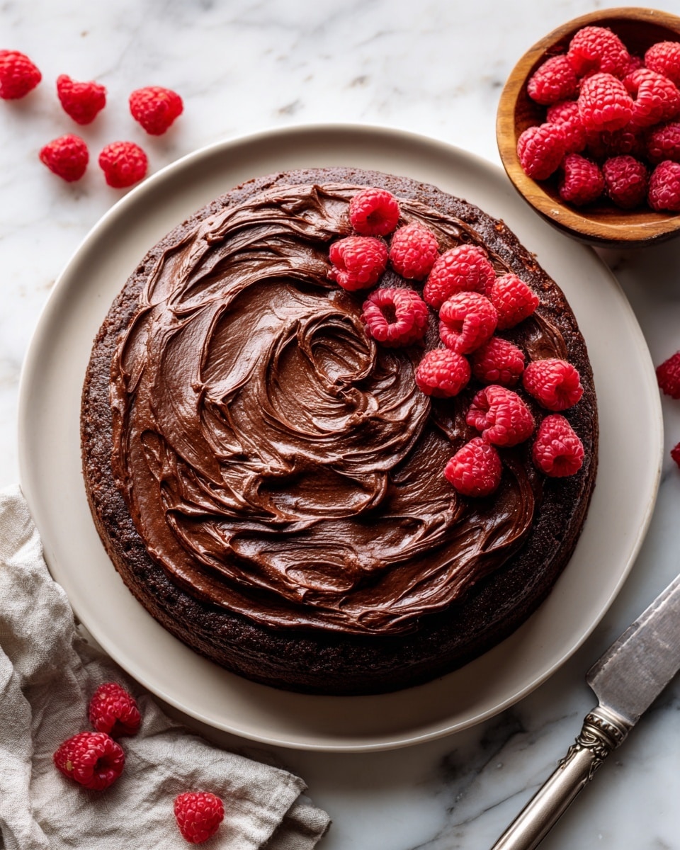 The image shows a single slice of chocolate cake on a white plate with a thin brown rim, placed on a white marbled surface. The cake slice has one thick dark brown base layer and a thick layer of smooth, textured chocolate frosting spread unevenly on top. There is one bright red raspberry sitting on the frosting, with two more raspberries beside the cake on the plate. A silver fork rests near the bottom edge of the plate, pointing slightly upward. In the upper right corner, there is a white bowl filled with more fresh raspberries. photo taken with an iphone --ar 4:5 --v 7