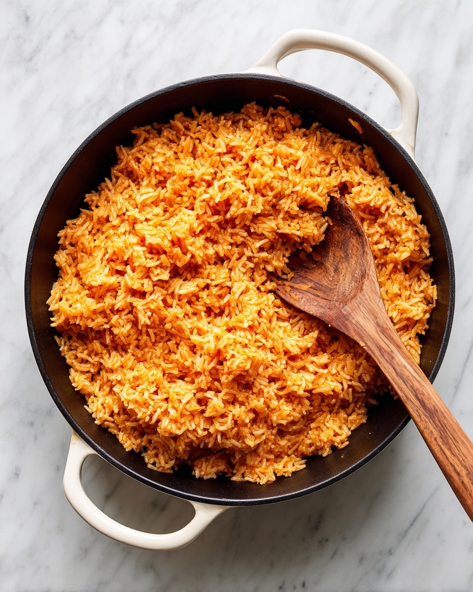 A cast iron skillet with two white handles filled with orange-colored rice is shown. The rice looks well mixed and fluffy, with each grain separate and coated with the orange sauce. A wooden spoon stirs the rice from the center, lifting some grains. The skillet sits on a white marbled surface. The texture of the rice appears soft yet firm, with a slight sheen from the sauce. photo taken with an iphone --ar 4:5 --v 7