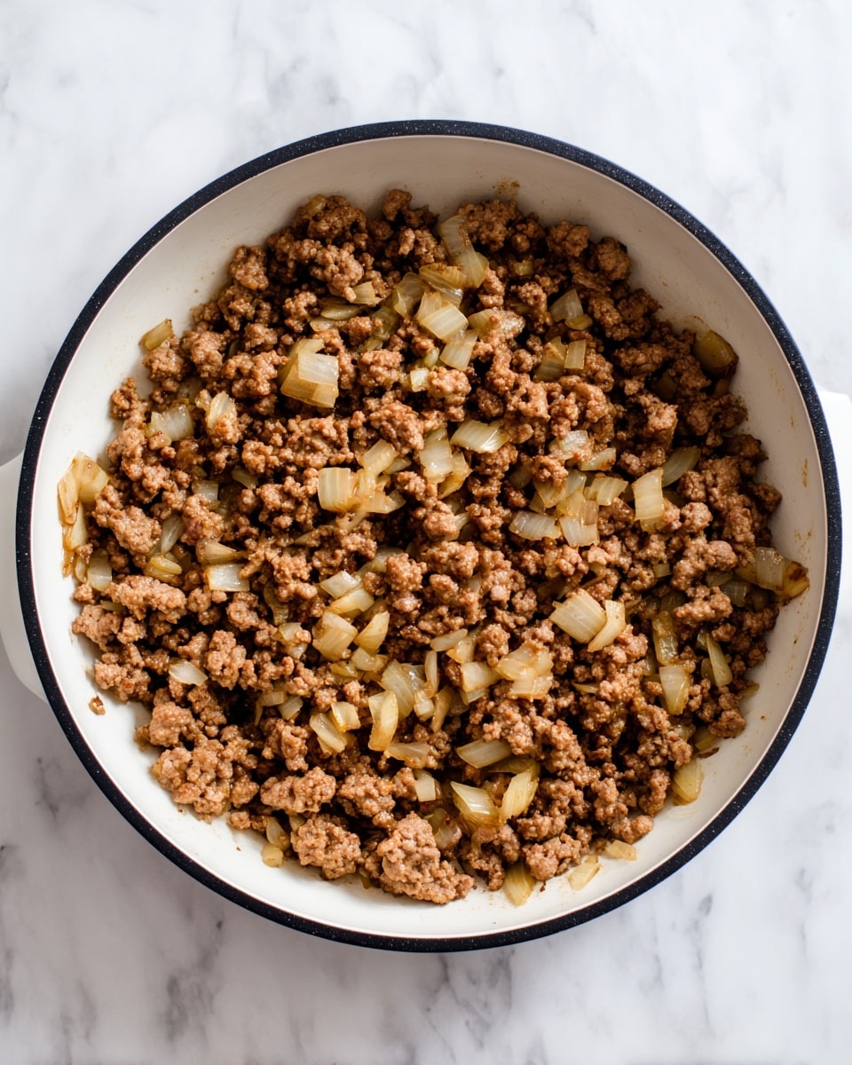 The image shows a white pan with a black rim sitting on a white marbled surface, filled with cooked ground meat mixed with light golden diced onions. The meat is brown and crumbly, covering most of the pan, with the onions scattered evenly throughout. There are small bits of cooked onion visible in the spaces between the meat. The pan has a smooth white interior and is viewed from above, showing the texture and color contrast between the browned meat and the pale onions. photo taken with an iphone --ar 4:5 --v 7