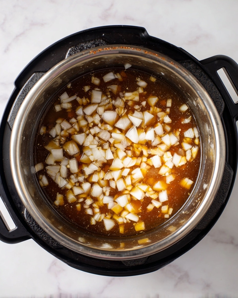The image shows a top view of a metal pot inside a black pressure cooker with diced white onions mixed in a light brown liquid. The onions are cut into small, uneven cubes and spread evenly across the bottom layer, with the liquid giving a shiny texture to the surface. The pot has some wear marks along the top rim, and the background is a white marbled texture. photo taken with an iphone --ar 4:5 --v 7