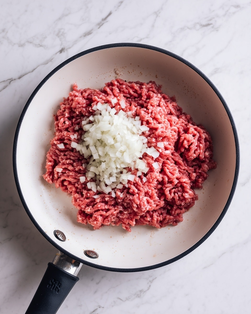 A white pan with a black edge sits on a white marbled surface, containing one thick layer of raw red ground meat in the center. On top of the meat, and spilling slightly to the right side, is a small pile of tiny, white chopped onion pieces, creating a contrast between the red meat and the white onion. The pan is clean aside from these two main ingredients. Photo taken with an iphone --ar 4:5 --v 7