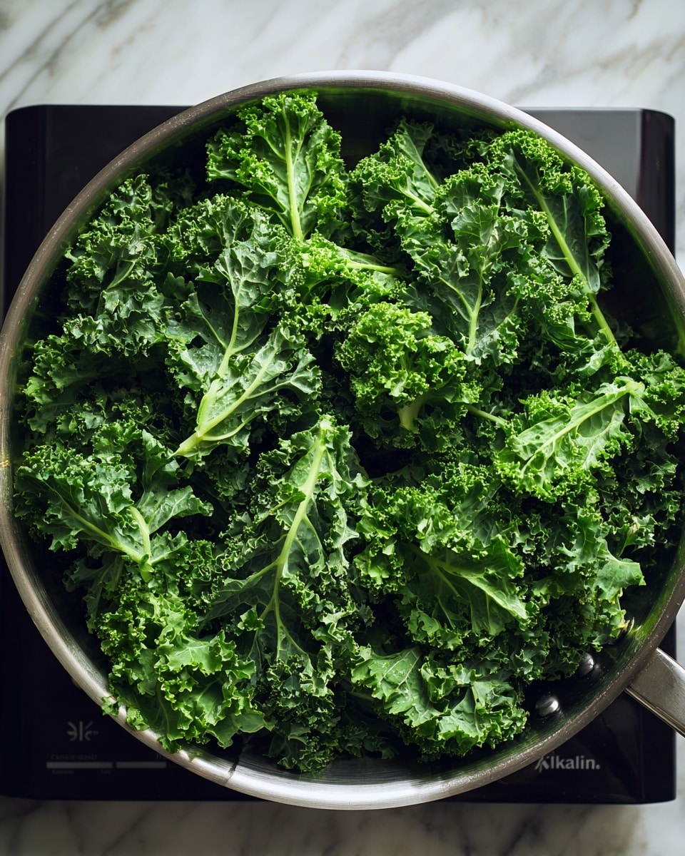 A shiny metallic pan sits on a black induction cooktop with the brand name visible, filled with fresh, bright green kale leaves. The kale is layered naturally with curly edges and visible veins, showing a mix of lighter and darker green shades. The background features a white marbled texture under the cooktop. photo taken with an iphone --ar 4:5 --v 7