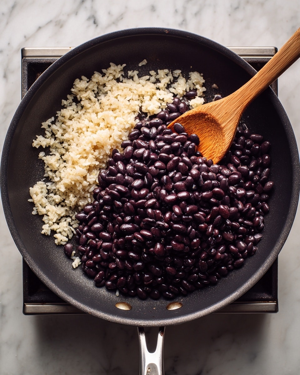 A black pan on a silver stove holds two main layers of food: the bottom layer is light beige small chopped pieces, soft in texture, spread across the left half of the pan; the top layer is a large mound of dark purple beans with a smooth, shiny texture, covering the right half of the pan. A wooden spatula is resting diagonally inside the pan, pointing from the bottom left to the top right. The stove and the area around it show a white marbled surface. photo taken with an iphone --ar 4:5 --v 7