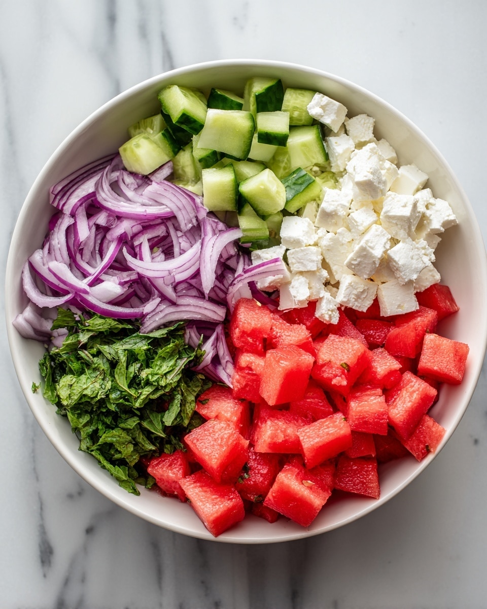 A white bowl is filled with five sections of fresh ingredients arranged side by side. Starting from the top left, there are small green cucumber cubes with a slightly glossy texture. Next to them, to the right, are white cubes of soft feta cheese, slightly uneven in size. Below the cheese, thin slices of purple-red onion with a smooth and shiny surface are spread in a small pile. To the left of the onion, bright green chopped mint leaves with a soft jagged texture add freshness. The largest section, taking up the bottom left half of the bowl, is filled with juicy red watermelon cubes with a slightly wet and shiny look. The bowl is placed on a white marbled surface. Photo taken with an iphone --ar 4:5 --v 7