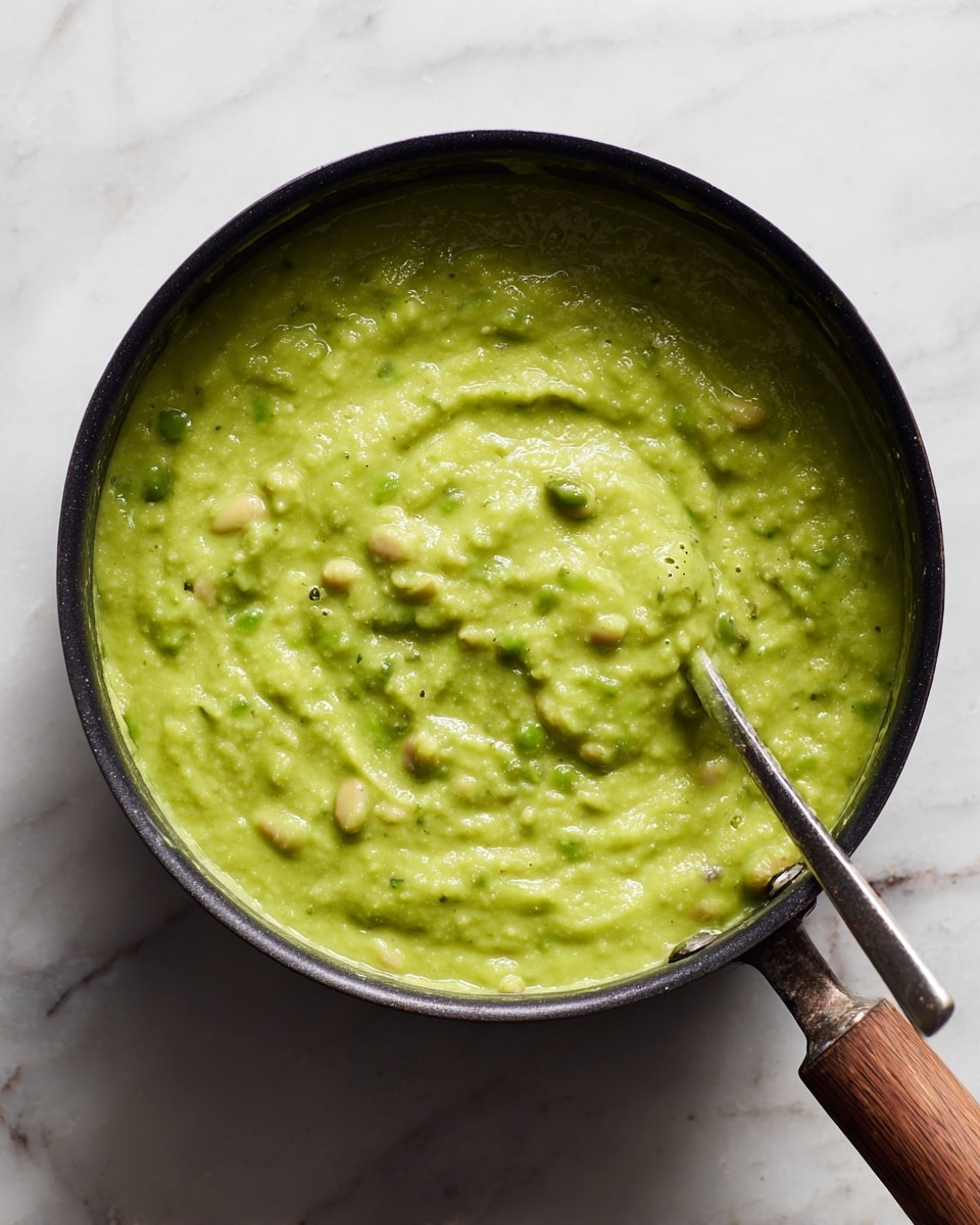 A close-up top view of a black pot filled with a thick, bright green creamy mixture that has visible rice grains and round beans throughout. The texture looks smooth and slightly chunky, with steam rising gently from the surface, showing it is hot. A utensil with a wooden handle and metal tip is partially submerged on the right side of the pot. The pot sits on a white marbled surface, adding a clean and bright contrast to the vivid green food. photo taken with an iphone --ar 4:5 --v 7