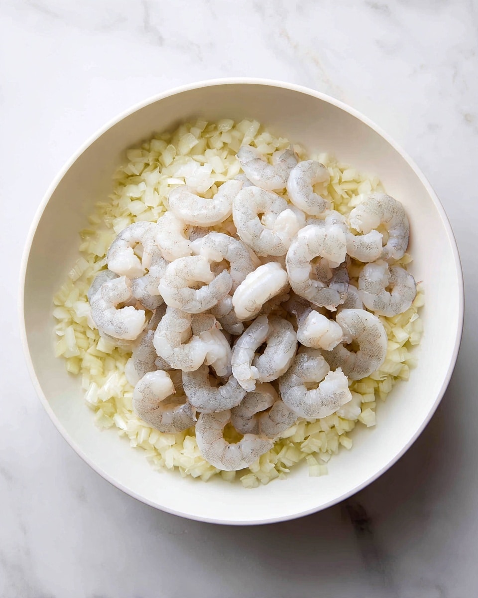 A white pan sits on a white marbled surface, filled with two layers: the bottom layer is small chopped light yellow onions, softened and spread evenly across the base, while the top layer consists of raw, peeled shrimp with a pale grayish-white color and slightly translucent texture, scattered in a loose pile over the onions, showing their curved shapes and subtle veins. Photo taken with an iphone --ar 4:5 --v 7