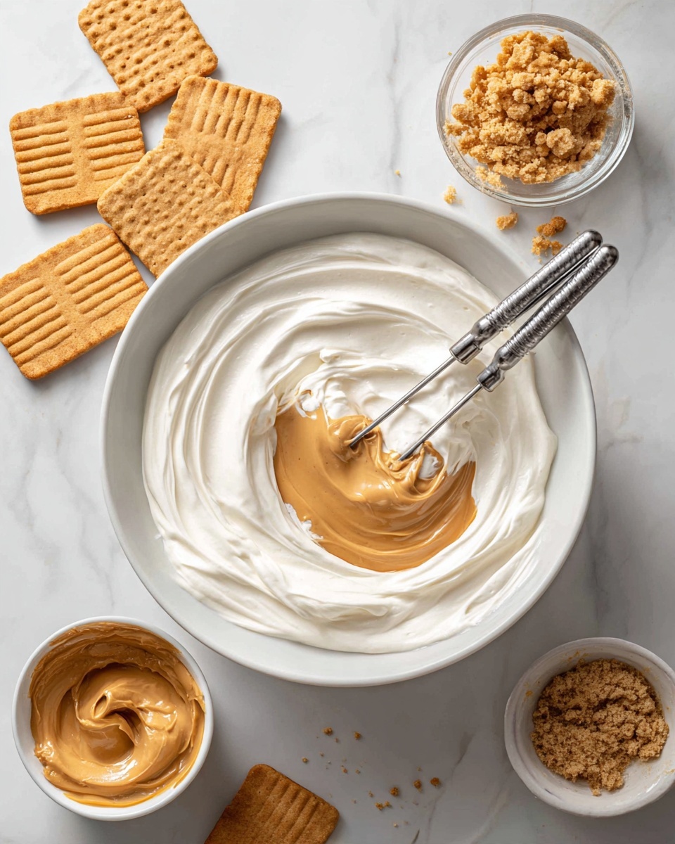 A white bowl sits on a white marbled surface, filled with two layers of creamy ingredients: a thick, smooth white cream spread around the bowl and topped with a dollop of light brown peanut butter in the center. Two silver beaters rest inside the bowl, partially dipped into the creamy mixture, showing soft swirls and folds of the two colors blending slightly. Surrounding the bowl are square-shaped golden brown cookies with a ridged pattern and small bowls containing creamy peanut butter and crushed cookie crumbs. Photo taken with an iphone --ar 4:5 --v 7