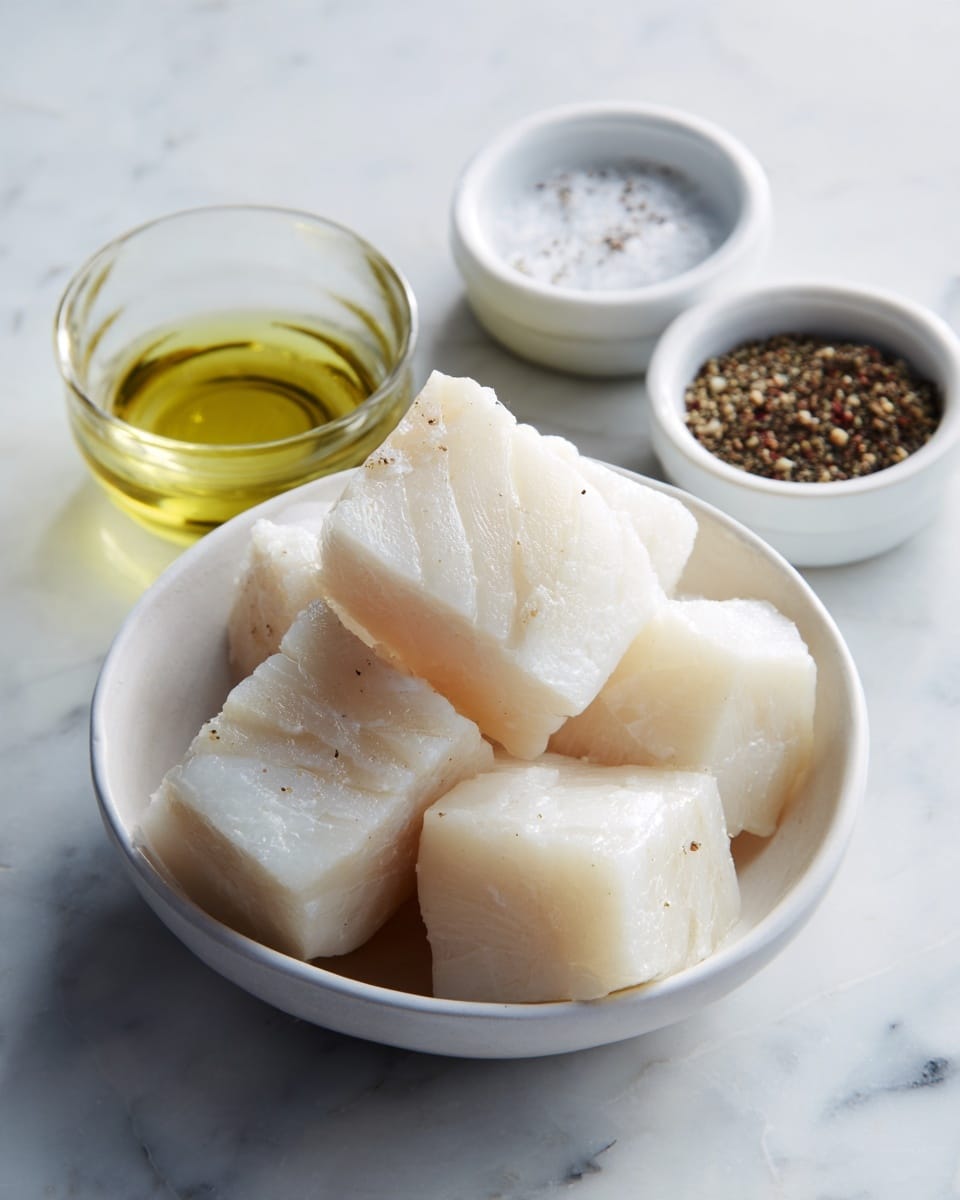 A ceramic white bowl filled with large, thick, white fish chunks, stacked unevenly showing soft and smooth shiny textures; behind and slightly to the left, a small white bowl holds salt and black pepper powders side by side, creating a split color pattern; next to it, a small clear glass cup contains light yellow cooking oil, all set on a white marbled surface. photo taken with an iphone --ar 4:5 --v 7