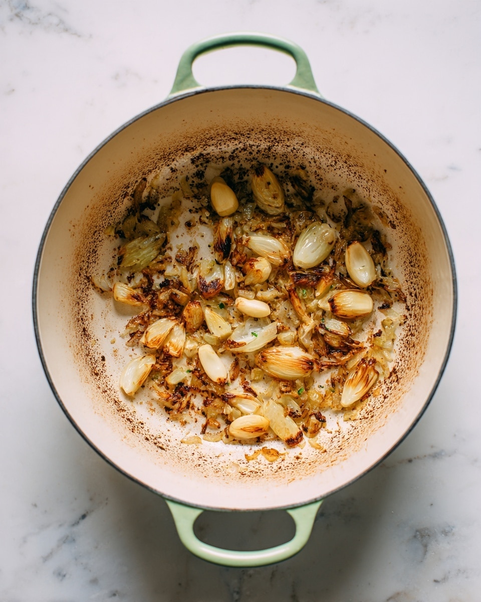 A round white pot with light green handles is placed on a white marbled surface. Inside the pot, there are pieces of cooked onions and whole garlic cloves spread around unevenly. The onions are soft and have a light brown color with some darker browned bits, showing they are fried or sautéed. The bottom of the pot shows brown residue from cooking, adding texture and depth to the image. The pot is empty except for these cooked pieces. Photo taken with an iphone --ar 4:5 --v 7