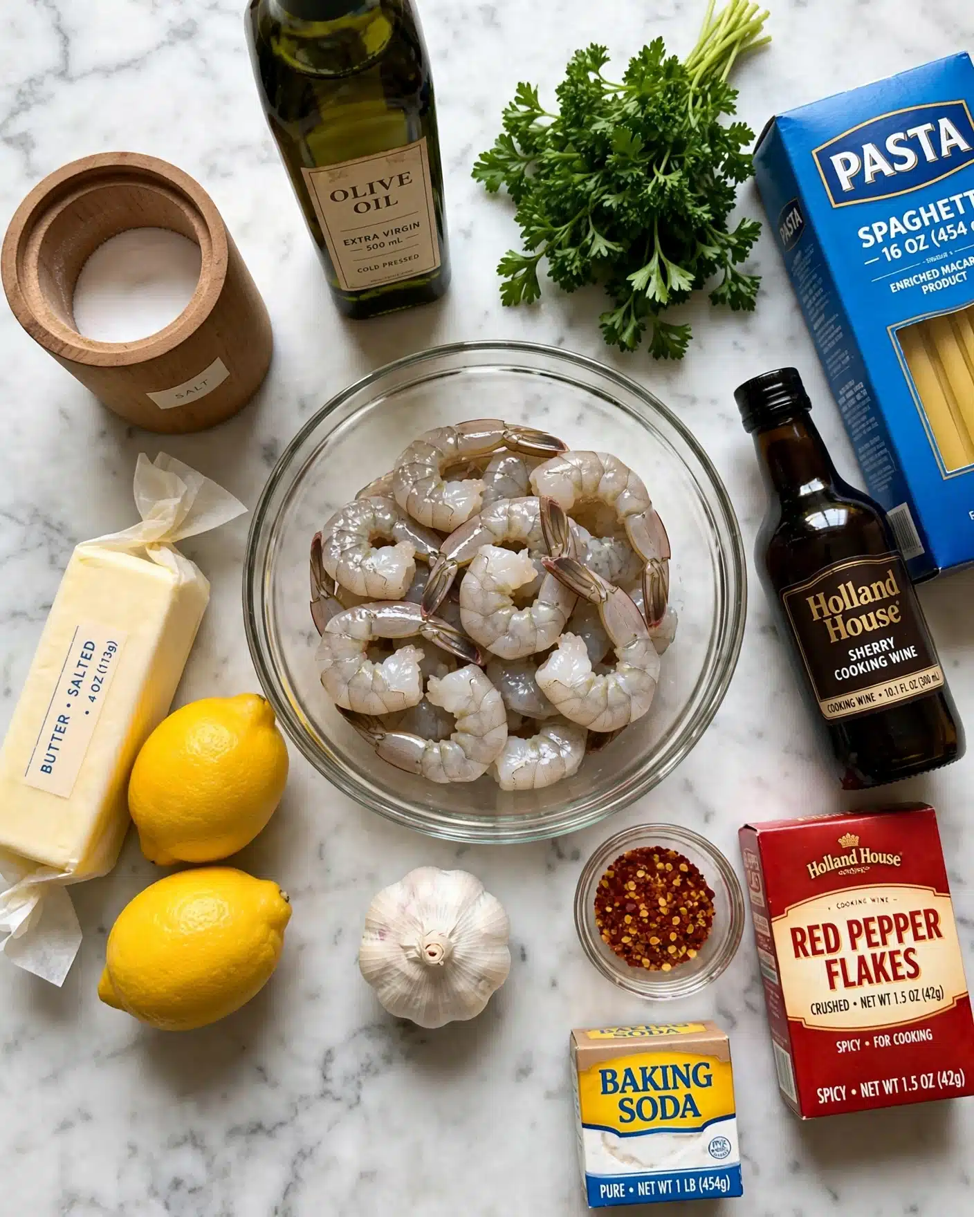 A clear glass bowl filled with raw shrimp sits on a white marbled surface, surrounded by various ingredients: a whole garlic bulb placed in front of the bowl, two bright yellow lemons next to a stick of butter wrapped in paper, a bunch of fresh green parsley with leafy texture, a cylindrical wooden container with a lid holding white salt, a bottle of olive oil, a dark brown bottle labeled Holland House sherry cooking wine, a box of red pepper flakes, red pepper flakes visible in a container, a box of baking soda, and a blue box of pasta. The arrangement is colorful with natural textures, all placed on the white marbled background. Photo taken with an iphone --ar 4:5 --v 7