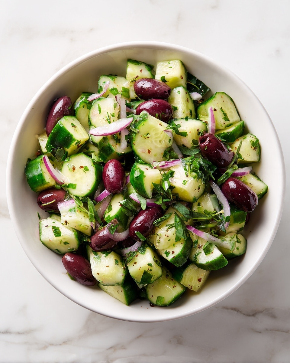 A white bowl filled with a fresh salad made of chopped cucumber pieces showing light and dark green skin, sliced deep red olives, and small bits of purple-red onion. The ingredients are mixed with small green herb leaves, evenly spread throughout. The bowl rests on a white marbled surface, and the overall look is bright with a mix of colors and textures from the smooth cucumber, firm olives, and soft onion pieces. photo taken with an iphone --ar 4:5 --v 7