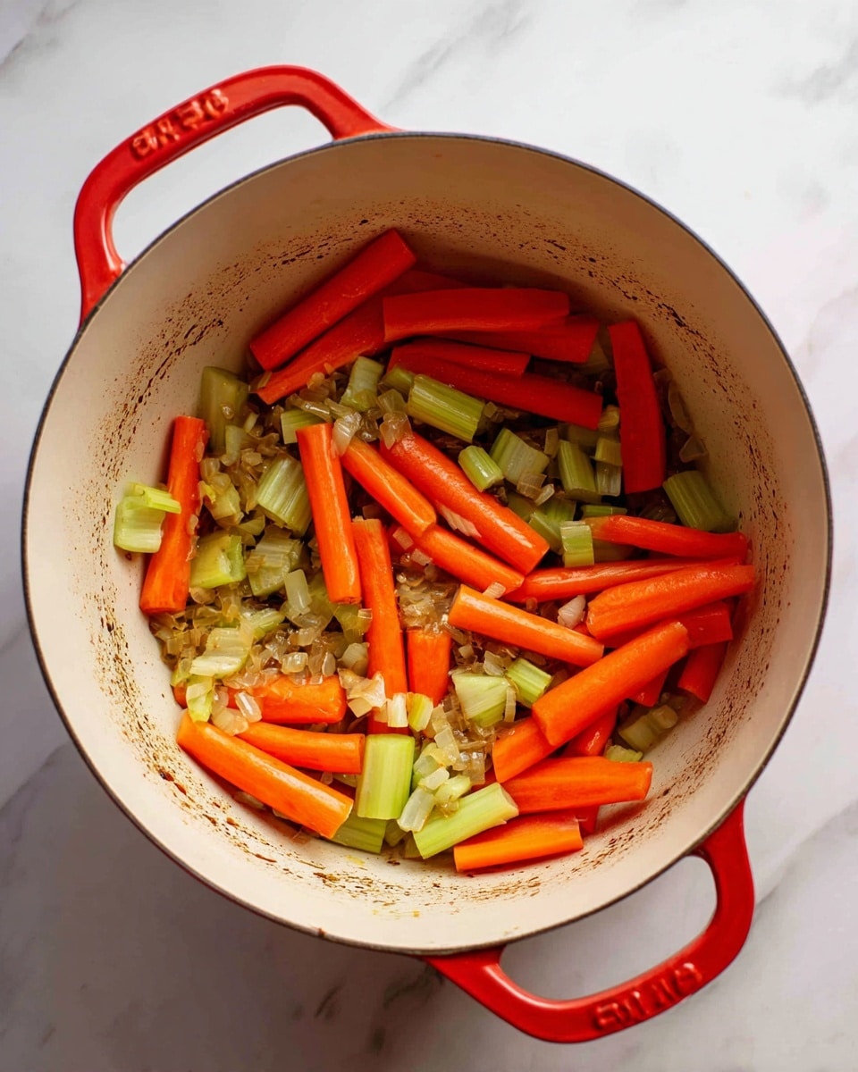 Inside a white pot with a red handle on a white marbled surface, there are three visible layers of cooked vegetables: bright orange carrot sticks, light green celery pieces, and small chopped light brown onions. The carrots are cut into thick sticks and spread evenly over the bottom of the pot. The celery pieces, smaller and slightly curved, are mixed with the carrots. The onions are finely chopped and scattered around, some showing a light golden-brown color from cooking. The inside of the pot shows some brown bits stuck to the surface from cooking. The photo taken with an iphone --ar 4:5 --v 7