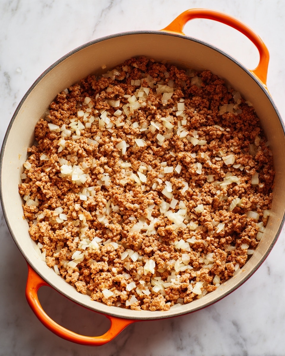 A close-up view of a large orange pot with a white inside, filled with browned ground meat mixed with small pieces of cooked onion scattered evenly throughout. The cooked meat looks crumbly and granular with a mix of light brown and slightly darker brown colors, while the diced onions are white and translucent. The pot sits on a white marbled surface. photo taken with an iphone --ar 4:5 --v 7